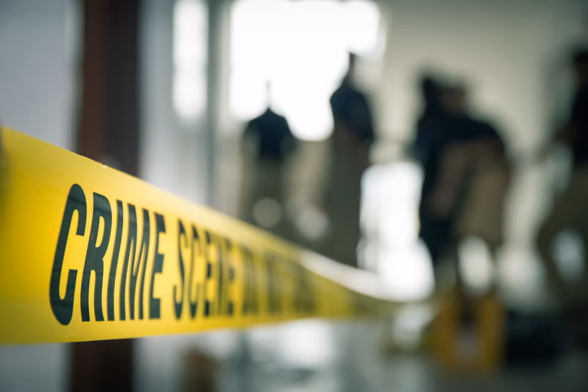 Crime scene DO NOT CROSS tape at a blurred out crime scene